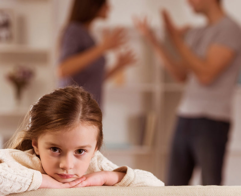 Child sitting on a couch as parents argue in the background